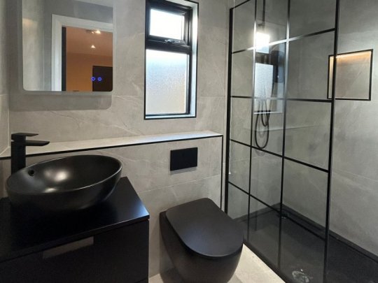 Modern bathroom design in Dublin featuring black sink, black toilet, black-framed shower, and stone ceramic tiles.