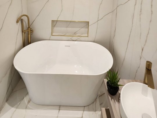 A stunning modern bathroom featuring a freestanding white bathtub, gold taps, and seamless large-format marble-effect wall tiling.