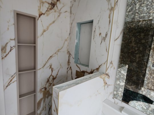 Luxurious bathroom renovation in progress featuring white marble with brown veining and recessed shelving, showcasing elegant tilework and modern design.