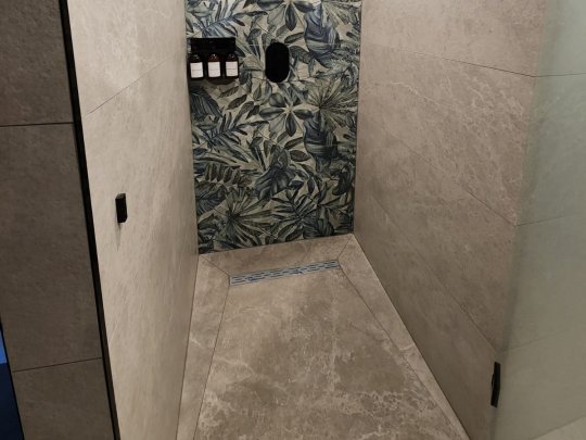 Close-up of a modern, textured grey anti-slip floor tile in a wet room shower with water droplets on the surface.