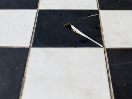 A close-up view of a hairline fracture running across a ceramic floor tile in a residential kitchen.