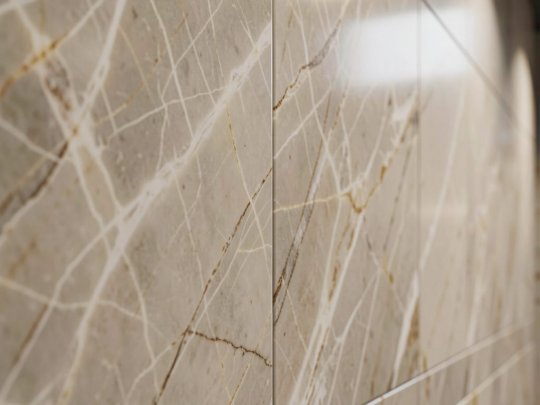 Close-up of polished marble-effect wall tiles with precise grout lines and sleek metal tile trim for a luxury bathroom finish.