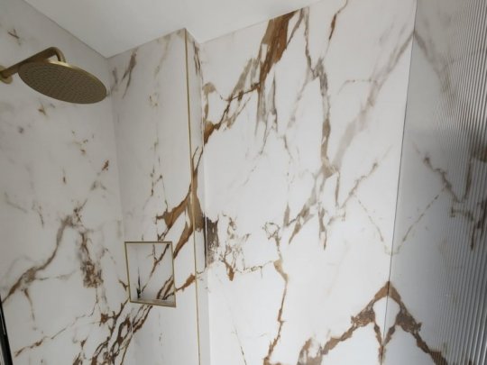 A modern luxury shower featuring large-format white marble tiles with gold veining, gold fixtures, and perfectly matched grout for a seamless finish.
