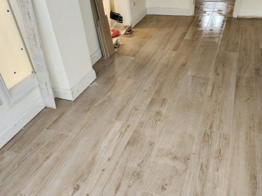 Newly installed light brown wood-effect porcelain floor tiles in a bright hallway, providing a durable and stylish flooring solution for a home.