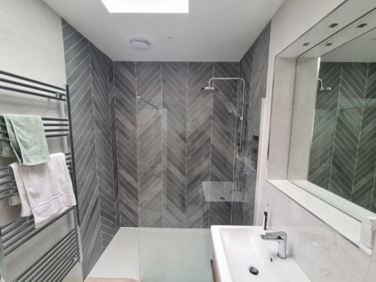 Contemporary walk-in shower featuring grey herringbone wall tiles and a minimalist glass screen, installed by RCTiling Dublin.