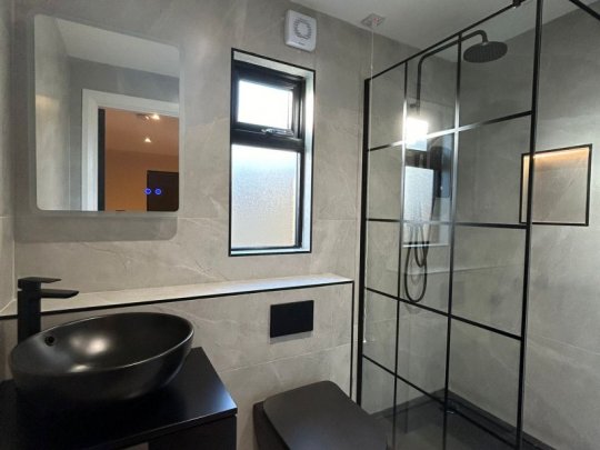 Modern compact bathroom in Dublin with large grey wall tiles, black fixtures, walk-in glass shower, floating black toilet, and matte black basin vanity.