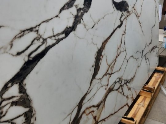 Large bookmatched marble-effect porcelain slab with bold dark veining, staged on wooden supports in a workshop.
