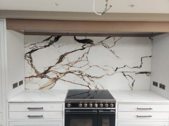 Modern Dublin kitchen installation featuring a dramatic white marble-effect porcelain slab splashback with bold black and gold veining, matching white countertops, white Shaker cabinets, and a premium range cooker.