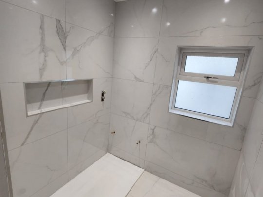 Modern minimalist bathroom with large-format marble-effect porcelain tiles, walk-in shower tray, recessed shower niche, and clean contemporary finishes.