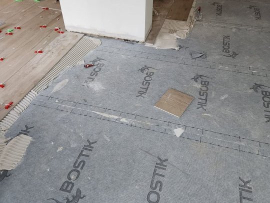 Bostik waterproofing membrane being installed on bathroom floor with notched adhesive and tile spacers visible during professional tiling preparation in Dublin