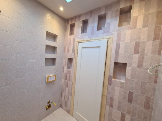 Modern tiled feature wall with decorative niches, textured hexagonal tiles, and vertical patterned wall tiles in a contemporary bathroom renovation.