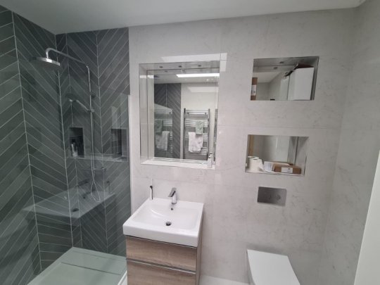 Modern Dublin bathroom featuring white marble-effect wall tiles, green herringbone shower tiles, recessed niches, and a contemporary vanity unit.