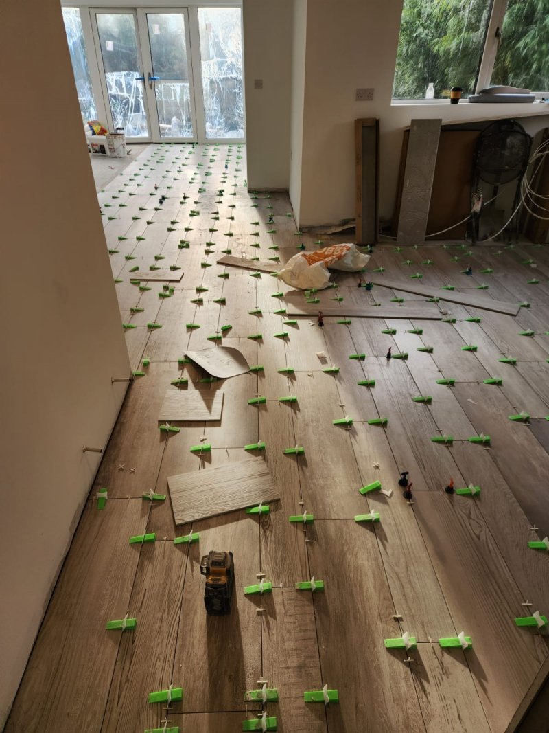 Professional tiling in progress, showing a tile levelling system and laser level being used to install wood-effect porcelain tiles.