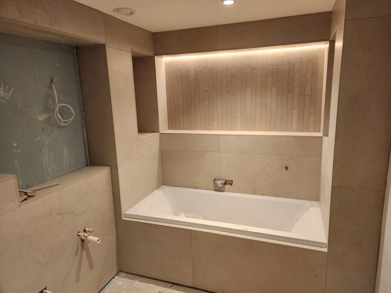 Bathtub wall with beige ceramic tiles and recessed niche during renovation – RC Tiling Dublin