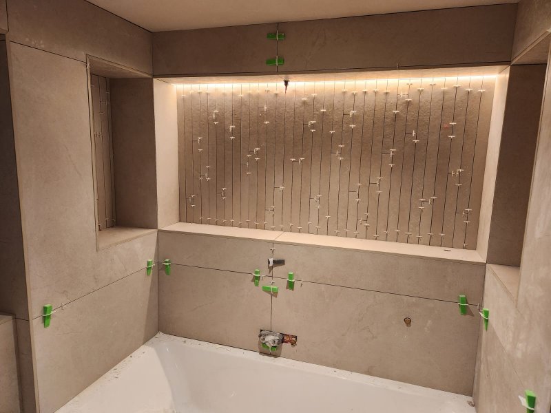 Modern bathroom tiling in progress by RCTiling Dublin, featuring a bathtub, vertical tile lines, LED lighting, and green spacers.