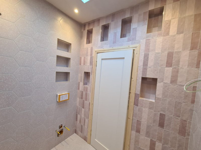 A wider view of a modern bathroom renovation, showcasing the harmonious combination of a hexagonal feature wall and walls tiled with vertically stacked rectangular tiles around a doorway.
