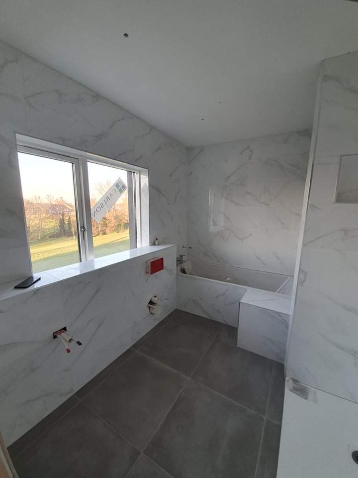 Modern bathroom renovation by RCTiling Dublin featuring glossy white marble-effect wall tiles and dark grey floor tiles with a tiled-in bathtub.