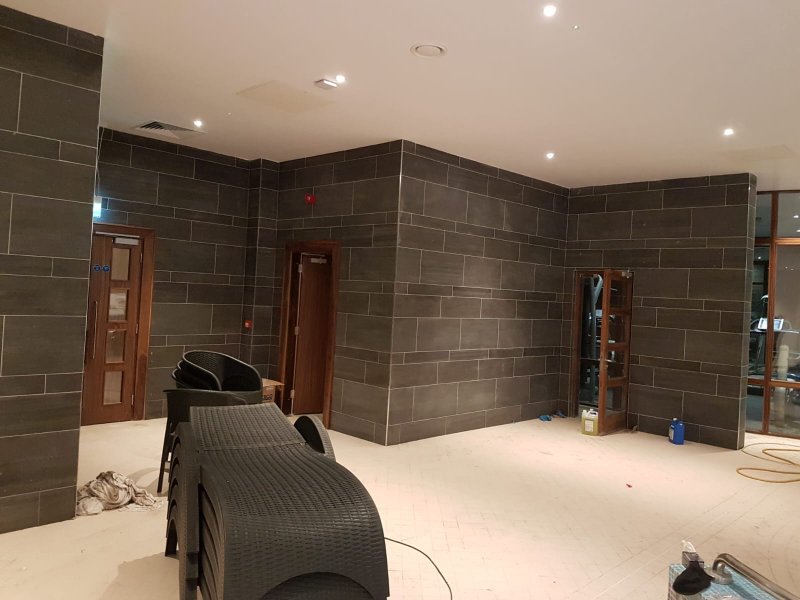 Precision wall tiling with large-format charcoal tiles in a commercial facility.